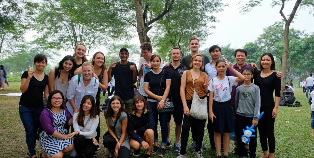 Group photo of international volunteers and Vietnamese participants during a VCV cultural exchange day in a park in Hanoi, smiling and standing together outdoors.