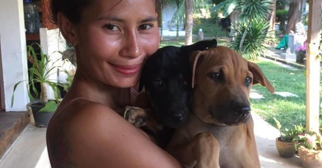 Smiling volunteer at Happy Dogs Koh Chang in Thailand holding two rescue puppies at the dog shelter.
