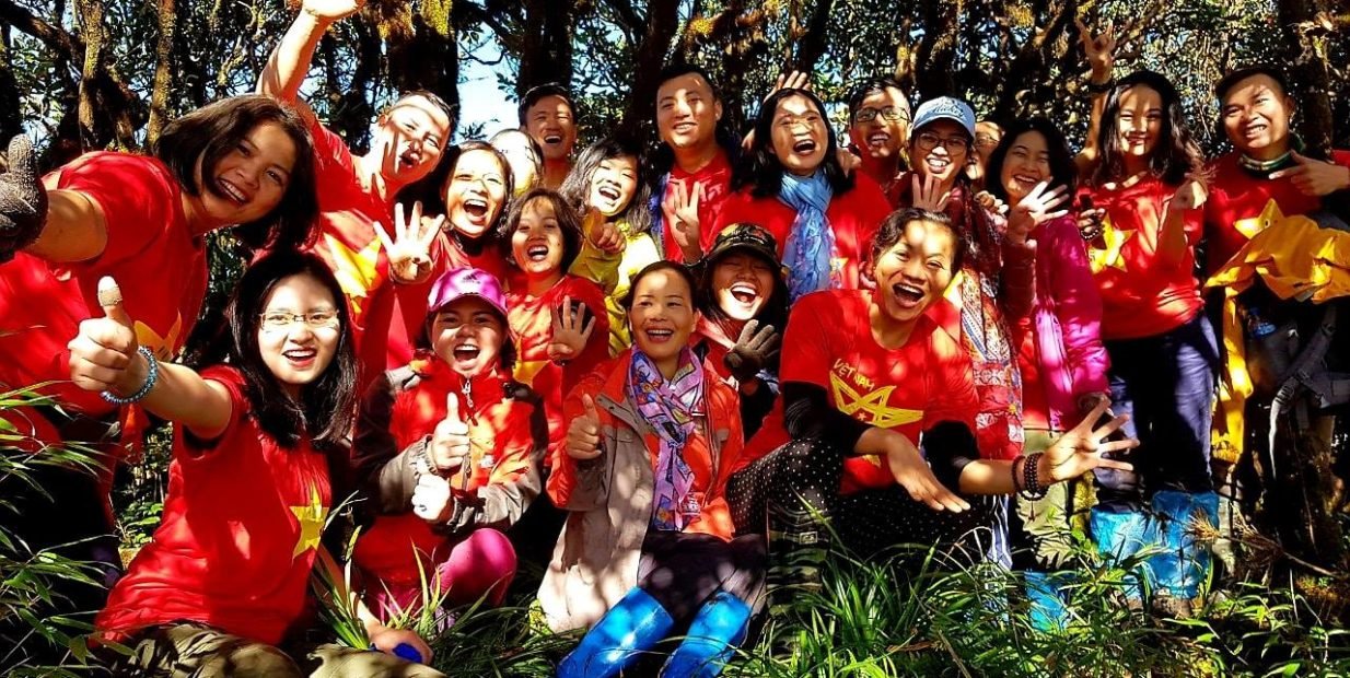 Smiling group of volunteers in red shirts outdoors in Vietnam, representing The5House Hanoi English volunteering program.