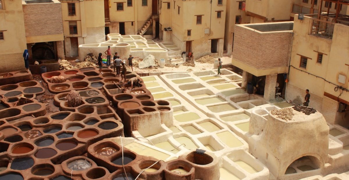 Traditional leather tanning pits in the ancient Medina of Fez, Morocco, with workers processing hides in colorful dye vats.