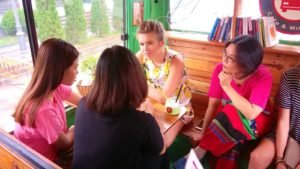 International volunteer teaching English in Hanoi café setting, engaged in conversation with local Vietnamese students as part of a cultural exchange program.