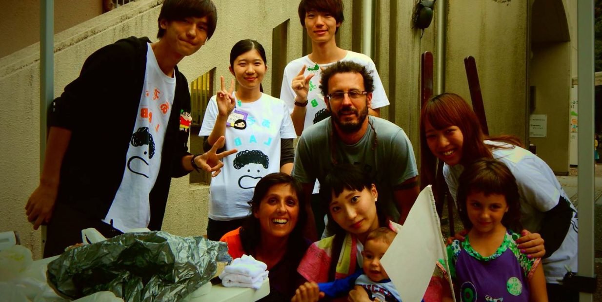 Nomadic family with two children posing with local volunteers at a community event during their 800-day slow travel and volunteering journey.
