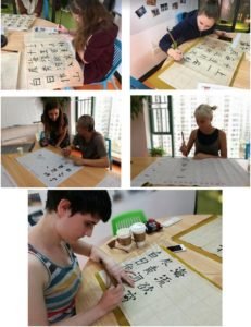 Qixing Au Pair China participants practice Chinese calligraphy during a Mandarin lesson in Shenzhen, learning brush strokes with teacher support.
