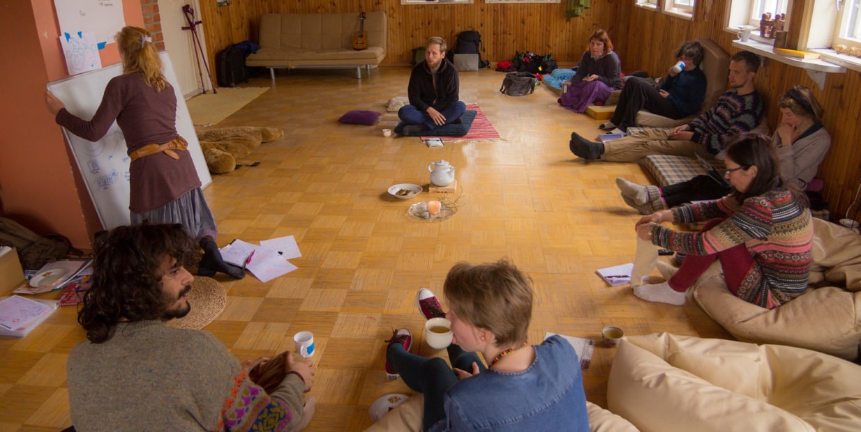 People sitting in a circle inside a cozy wooden room during a community workshop at an ecovillage in Estonia.
