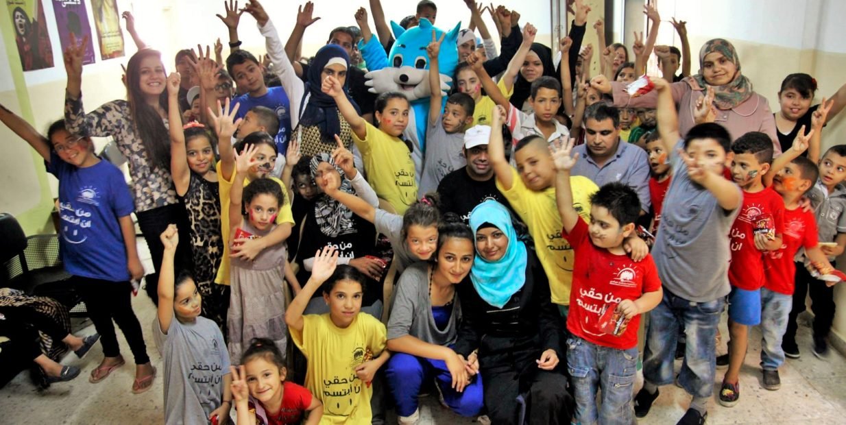 Group of children and volunteers at the Palestinian Society for Care and Development in Al Amari refugee camp, Palestine, participating in a community event promoting education, inclusion, and social care.