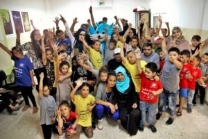 Group of children and volunteers at the Palestinian Society for Care and Development in Al Amari refugee camp, Palestine, participating in a community event promoting education, inclusion, and social care.