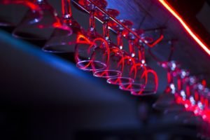 Hanging cocktail glasses under red lights in a lively Copenhagen bar where volunteers and staff work at the popular Copenhagen Downtown Hostel.