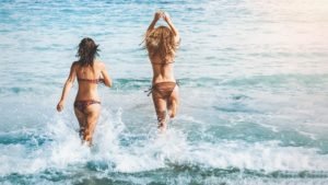 Two young women enjoying the sea during an eco-friendly beach holiday – sustainable travel and responsible tourism concept.