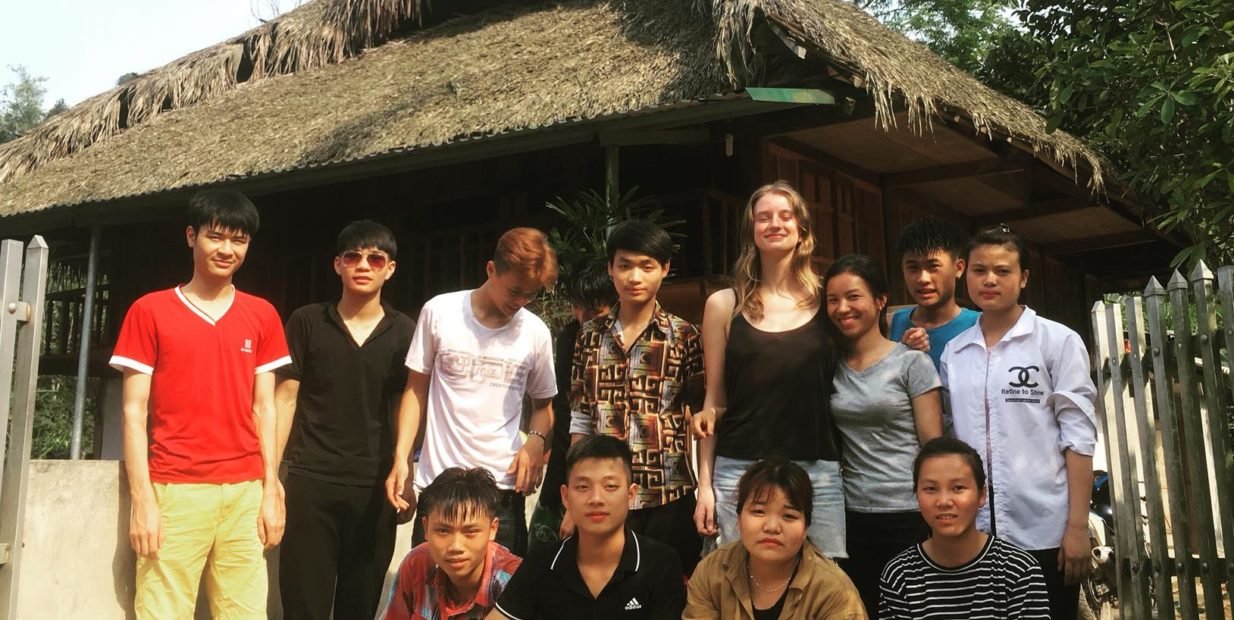 International volunteer and Vietnamese students outside a traditional house in Ha Giang while teaching English with Education for Ha Giang Highland Community, Vietnam
