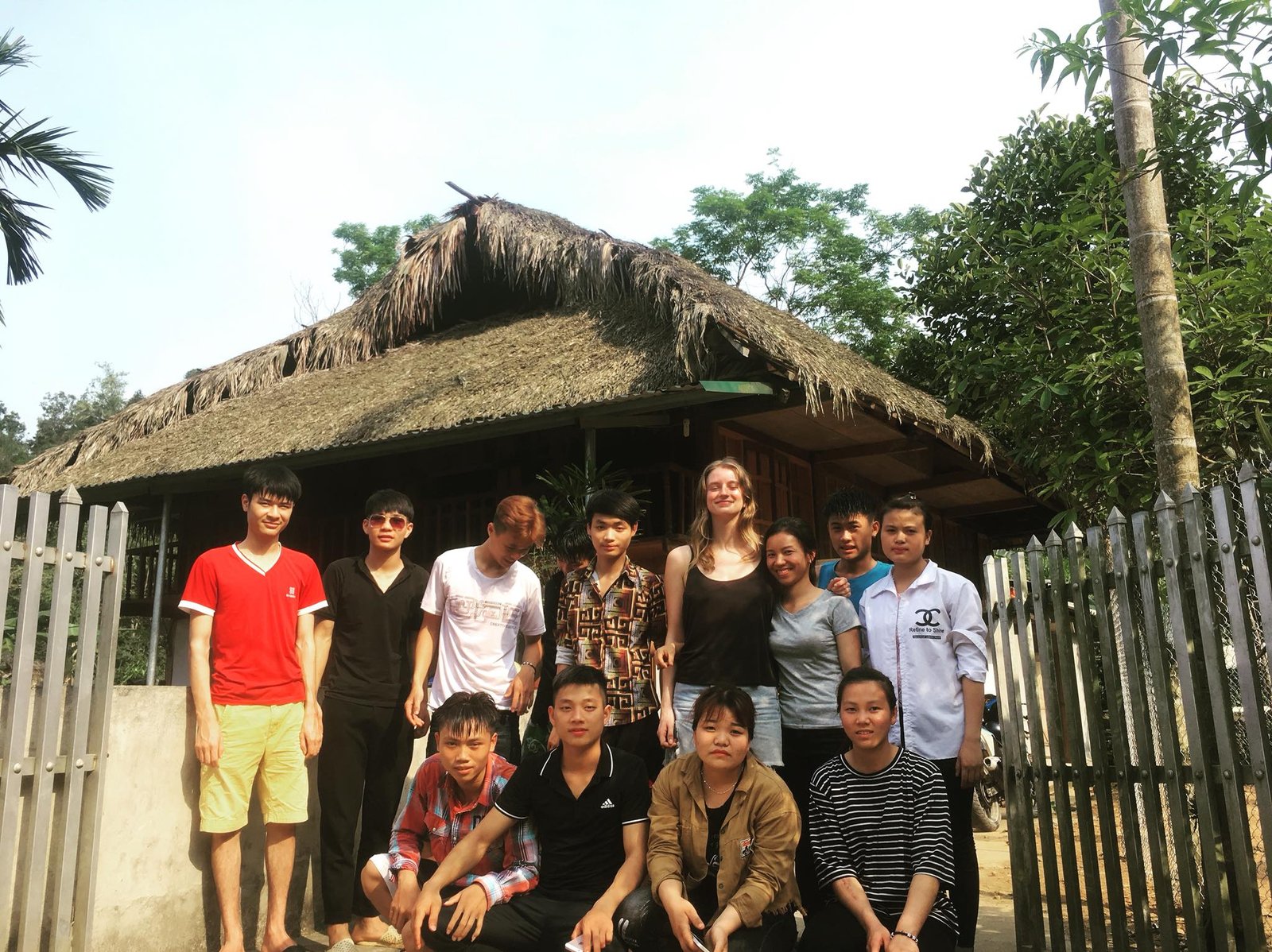 International volunteer and Vietnamese students outside a traditional house in Ha Giang while teaching English with Education for Ha Giang Highland Community, Vietnam