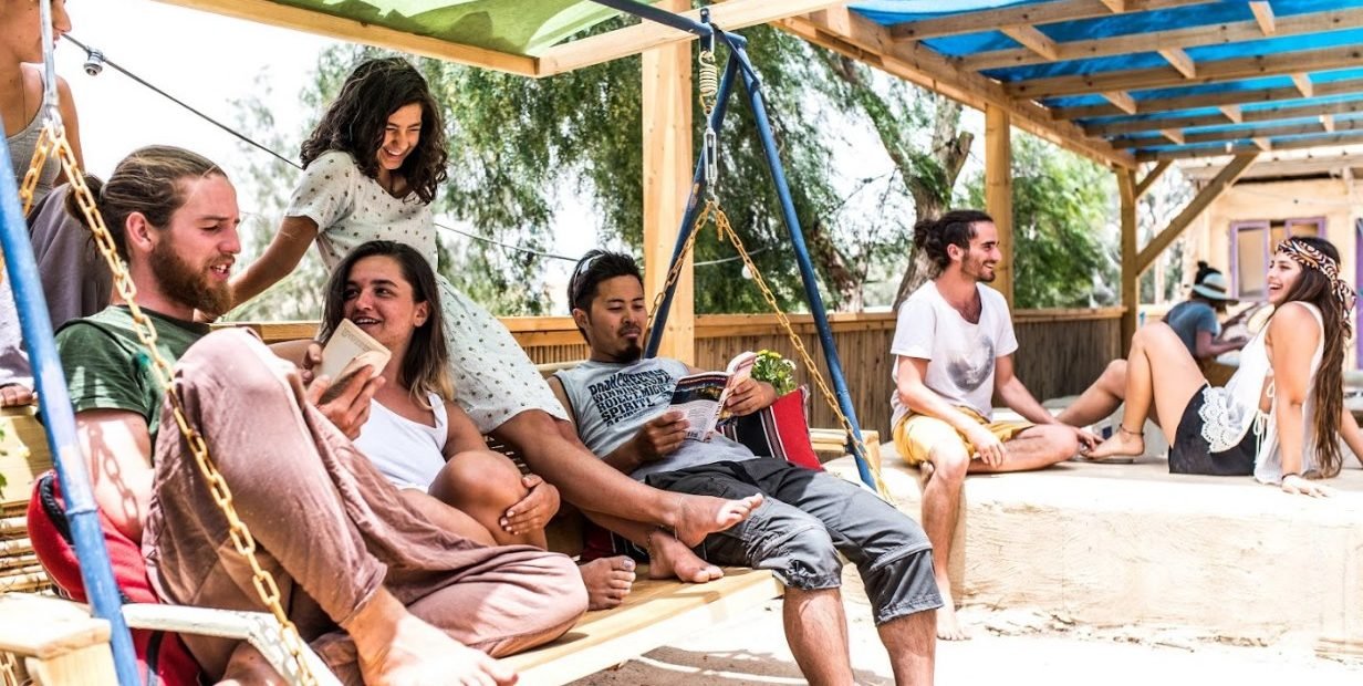 Group of young volunteers relaxing on a shaded swing and terrace at Meever eco-art community hostel in the desert town of Mitzpe Ramon, Israel.