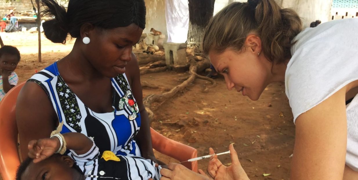 Medical volunteer in Ghana giving a vaccination to a baby while the mother holds the child during a community health outreach clinic.