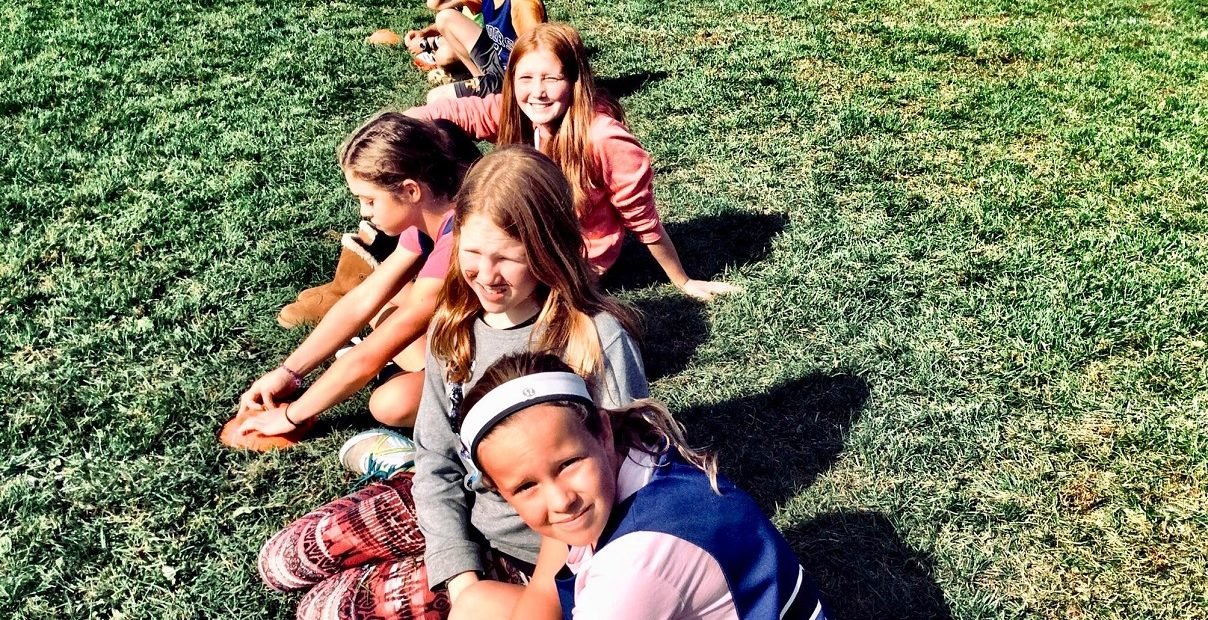 Teenagers sitting in a line on the grass during outdoor activities at an English summer camp in the lake region of northeast Poland