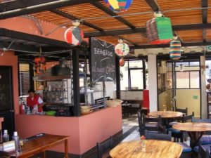 Open air café area at Hostel El Cafecito in Cuenca with wooden tables, bar and colourful decorations