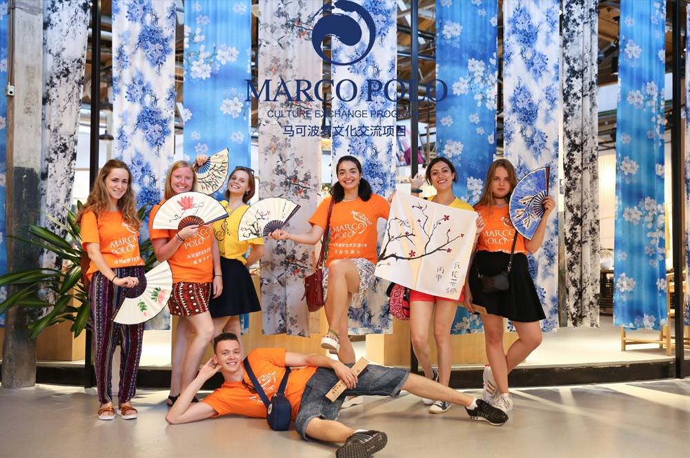 Group of international participants in orange T shirts holding fans at the Marco Polo Culture Exchange Program in Hangzhou, China, part of a pocket money au pair and cultural exchange experience.