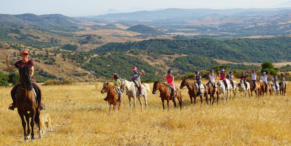 Group of riders on horseback crossing a golden hillside near Casares in Andalusia, Spain, during a rescue horse volunteering experience with Riding Fun In The Sun.