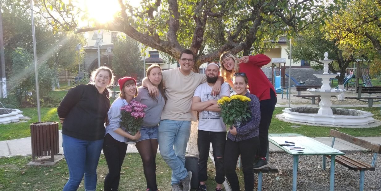 Group of young European volunteers smiling and holding flowers in a garden in rural Izvoarele, Romania, during an ESC cultural project.