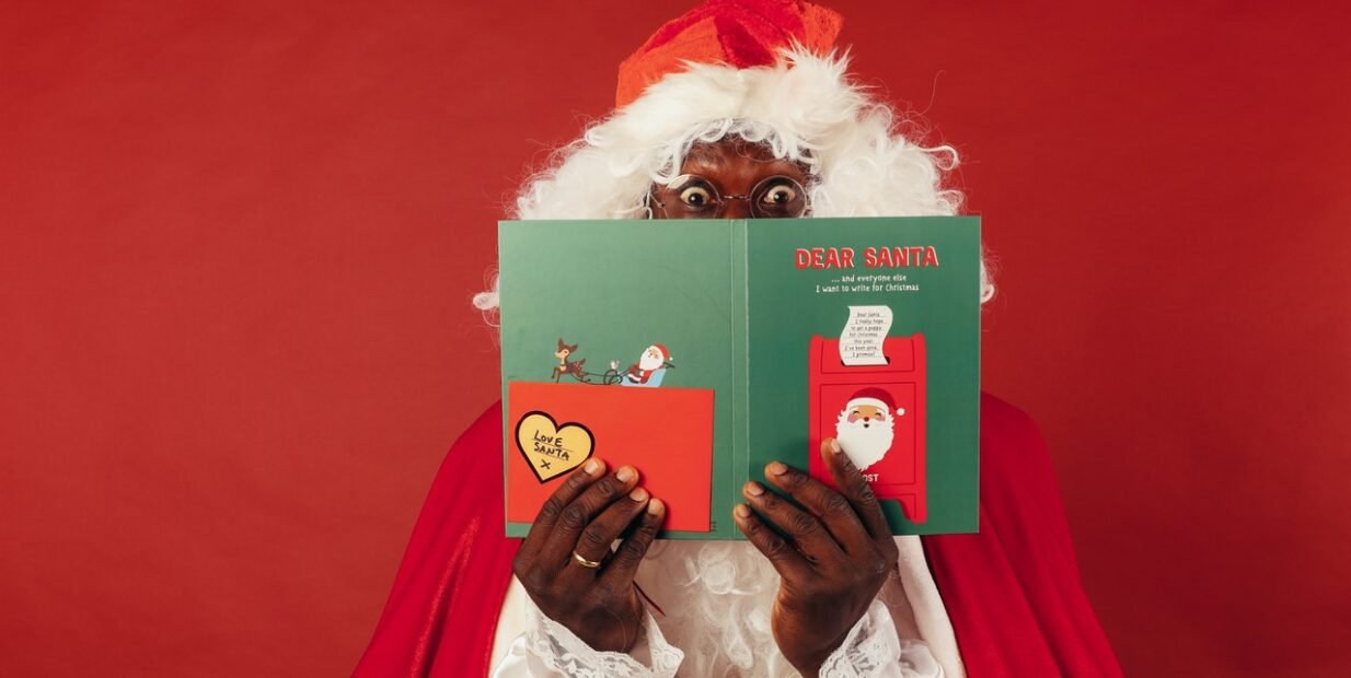 Surprised Santa Claus holding a colourful “Dear Santa” Christmas card on a red background, fun image for a guide on how to say Merry Christmas in different languages around the world.