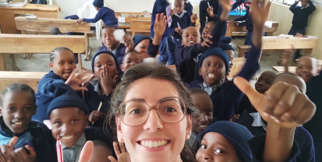 A smiling volunteer takes a selfie with a joyful group of school children inside a classroom at Tabasamu Orphanage, Arusha, Tanzania.