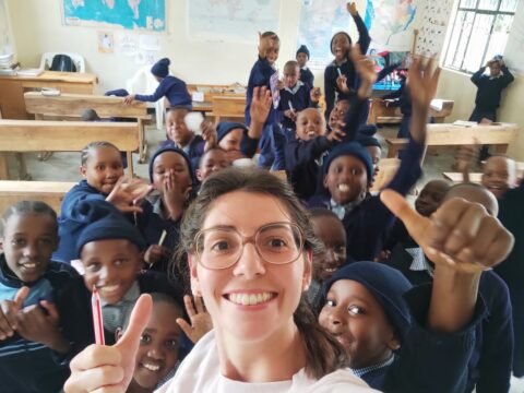 A smiling volunteer takes a selfie with a joyful group of school children inside a classroom at Tabasamu Orphanage, Arusha, Tanzania.