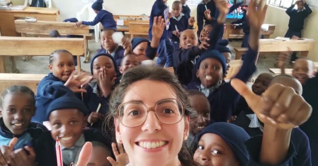 A smiling volunteer takes a selfie with a joyful group of school children inside a classroom at Tabasamu Orphanage, Arusha, Tanzania.