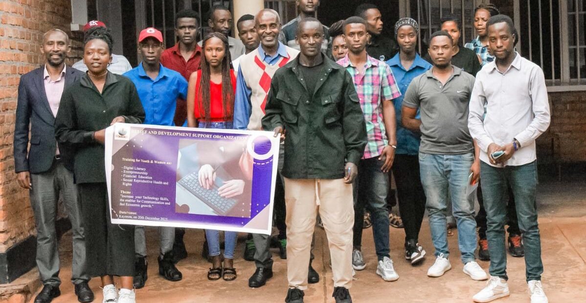 A group of young adults in Rwanda pose for a group photo during a training event, holding a banner about digital literacy, entrepreneurship, and youth empowerment.