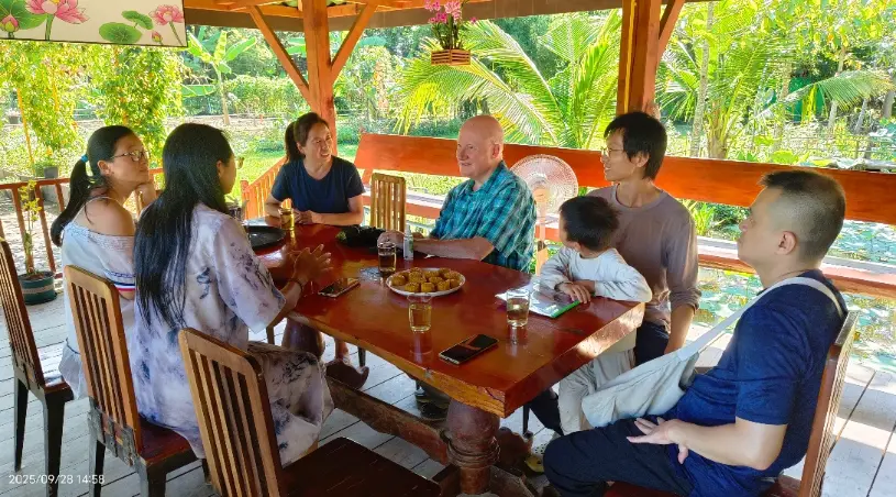 Volunteers and community members sitting together around a wooden table at Life Chanyuan ecovillage in northern Thailand, sharing tea and conversation.