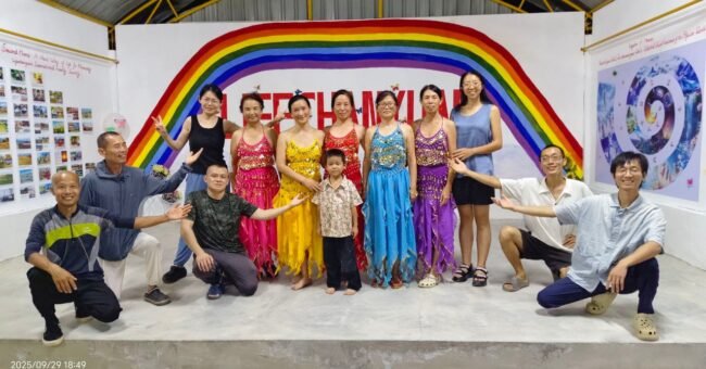 Lifechanyuan International Family Society Thailand Branch community members and volunteers standing together in front of a rainbow mural at their ecovillage.