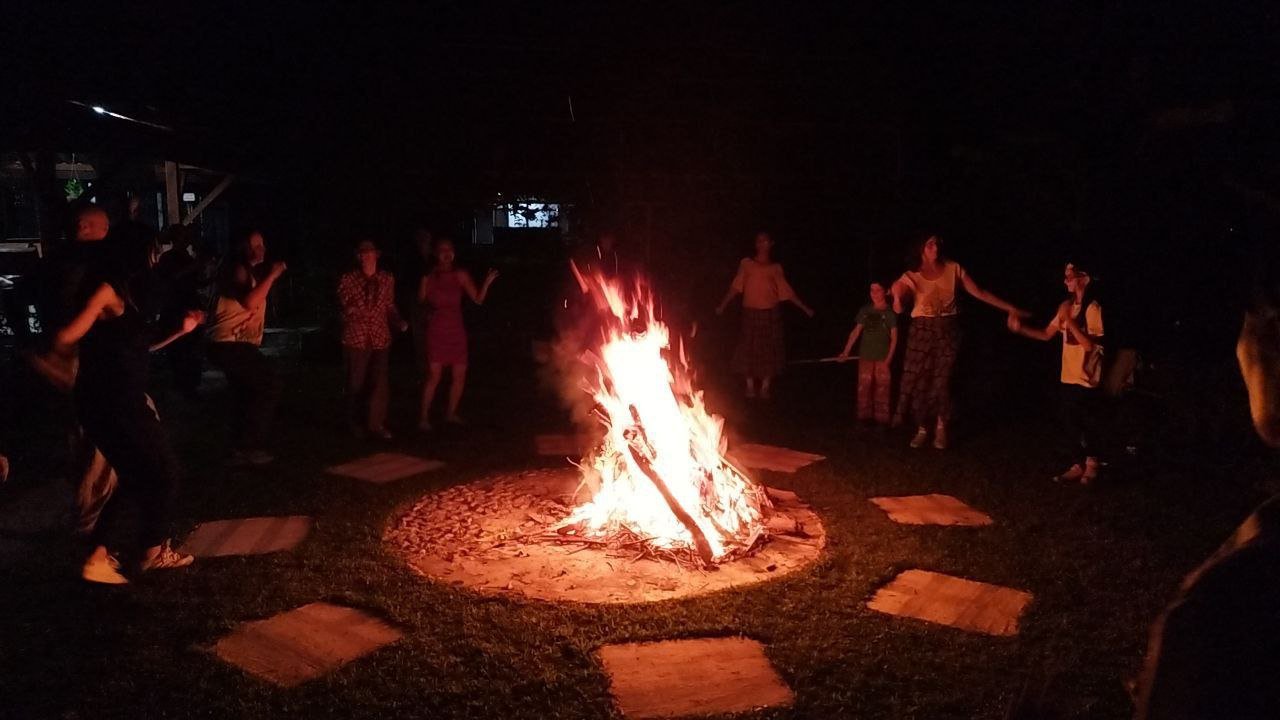 Volunteers and community members dancing in a circle around a bonfire at night at Lifechanyuan ecovillage in northern Thailand.