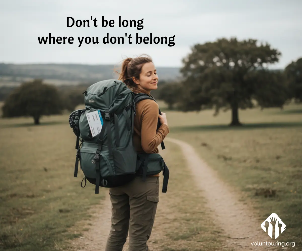 Smiling backpacker standing on a country path with a large green hiking pack, turning back toward the camera in an open field with trees. Quote reads, “Don’t be long where you don’t belong.”