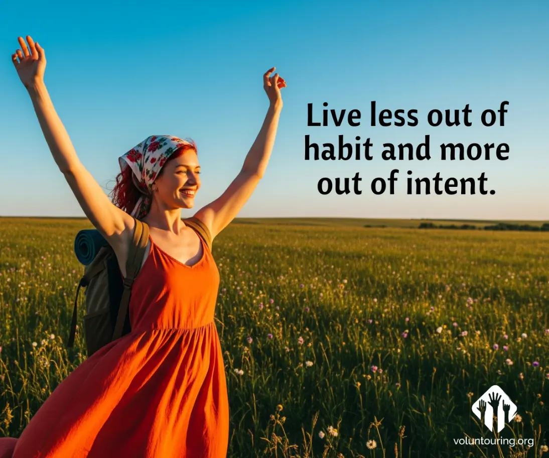 Smiling woman in an orange dress with arms raised, wearing a backpack and floral headscarf, standing in a green field at sunset with the quote 'Live less out of habit and more out of intent'.