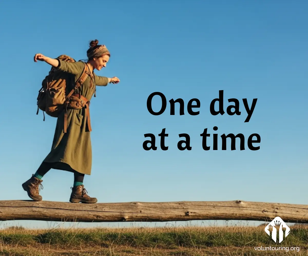 A young traveler with a large backpack balances playfully on a wooden fence under a clear blue sky, with the words "One day at a time" written beside them.