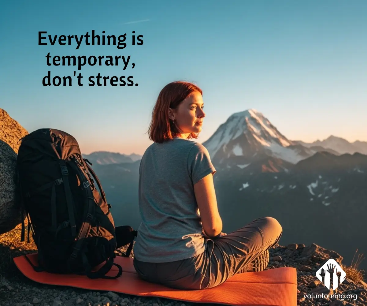 Woman sitting on a mountain peak at sunrise with a backpack, gazing at the distant snow-capped summit. Text reads "Everything is temporary, don't stress." Inspirational travel quote by Voluntouring.org.