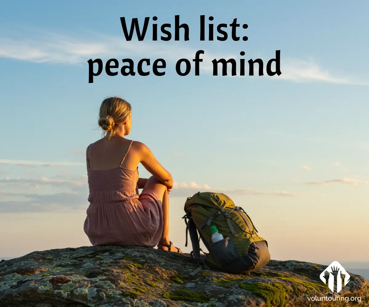 A woman sits peacefully on a rocky mountaintop at sunset with a backpack beside her. The sky is clear and calm. Text reads: 'Wish list: peace of mind'. Logo of voluntouring.org is visible in the corner.