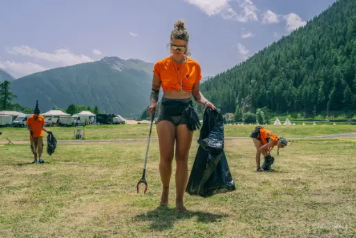 Psyclean volunteer cleaning a festival field with a trash picker and garbage bag in the mountains of Europe.