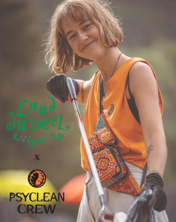 Smiling Psyclean Crew volunteer wearing gloves and using a trash picker at Landjuweel Festival, promoting environmental cleanup with joy and purpose.