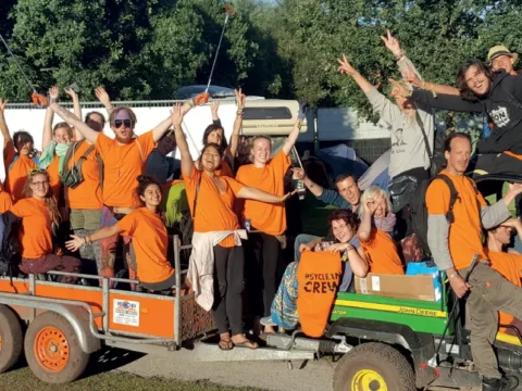 Group photo of Psyclean crew volunteers in bright orange shirts celebrating at a European music festival cleanup mission.