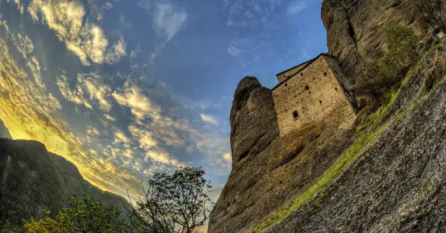 A dramatic view of the Castello della Pietra (Castle of the Stone) built into a rocky cliffside in Vobbia, Liguria, Italy, at sunset.