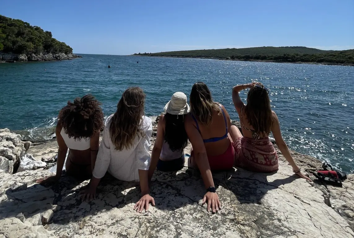 international village volunteer Poland - Group of volunteers sitting by the sea under the sun, smiling and chatting — likely part of a youth cultural camp in Europe.