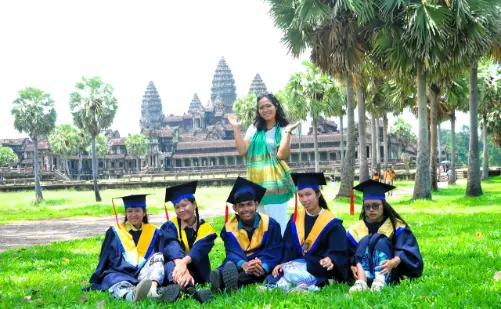 AHHA Education students in graduation robes posing in front of Angkor Wat, Cambodia, with a teacher standing behind them smiling.