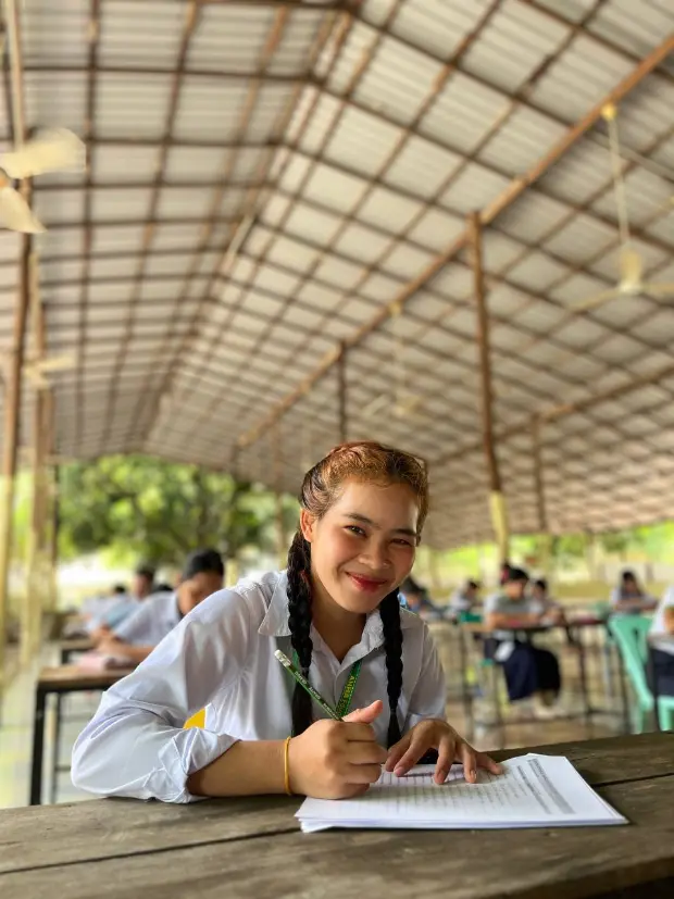 Smiling Cambodian student writing in her notebook during an outdoor class at AHHA Education in Kampot.