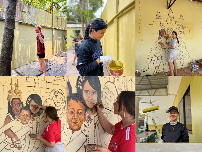 Volunteers and students painting a large mural on yellow walls at AHHA Education in Cambodia, using rollers and brushes to create portraits and cultural designs.