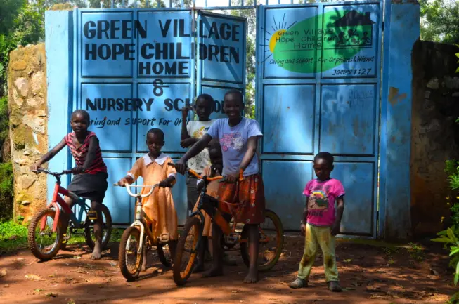Children with bicycles at the blue entrance gate of Green Village Hope Children Home and Nursery School in Vihiga, Kenya.