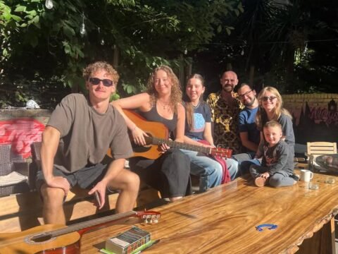 Saint James Backpackers volunteers relaxing in the London hostel garden on a sunny day, guitars on the table, friendly international team atmosphere.