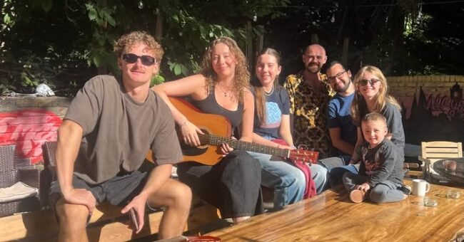 Saint James Backpackers volunteers relaxing in the London hostel garden on a sunny day, guitars on the table, friendly international team atmosphere.