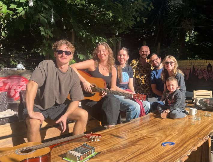 Saint James Backpackers volunteers relaxing in the London hostel garden on a sunny day, guitars on the table, friendly international team atmosphere.