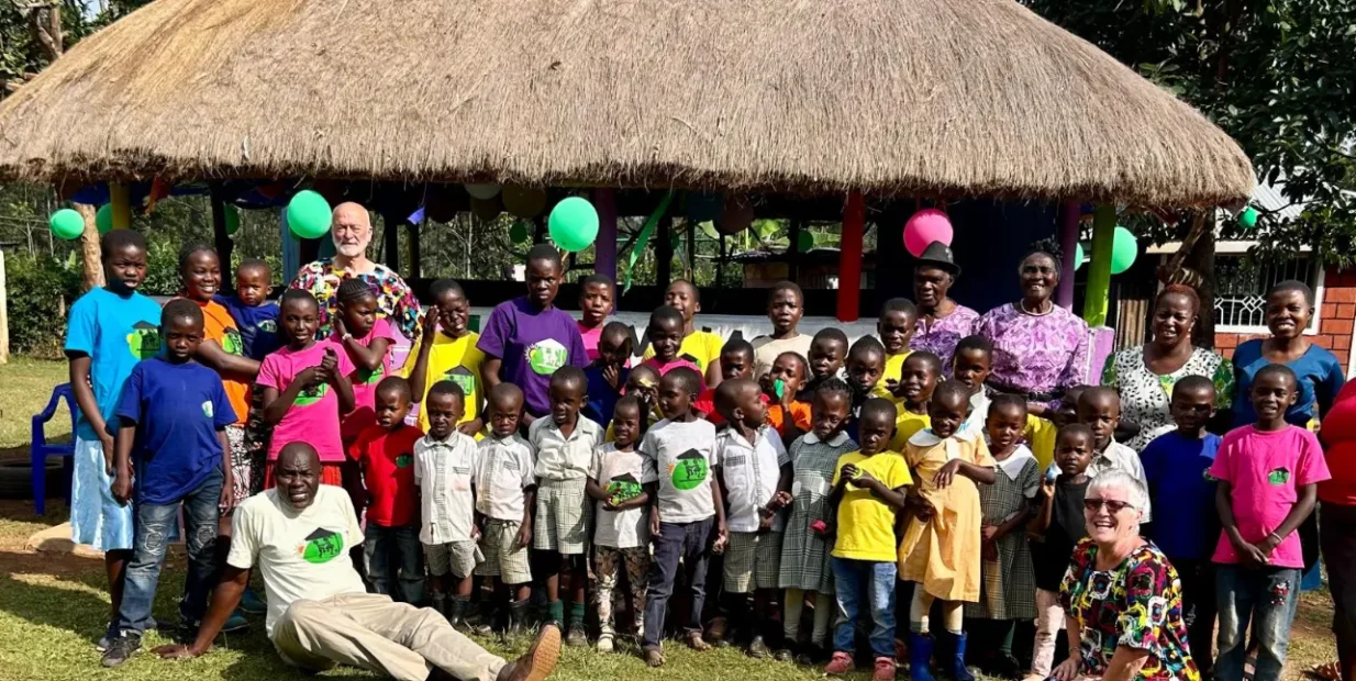 Volunteers and children at Green Village Hope Children Home in Vihiga, Kenya, group photo outside a thatched gazebo during a community day.