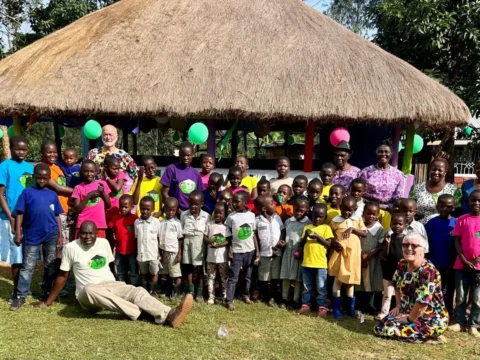 Volunteers and children at Green Village Hope Children Home in Vihiga, Kenya, group photo outside a thatched gazebo during a community day.