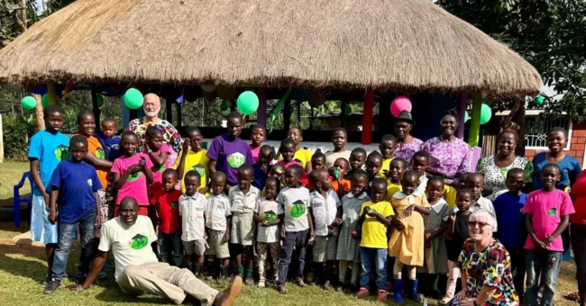 Volunteers and children at Green Village Hope Children Home in Vihiga, Kenya, group photo outside a thatched gazebo during a community day.