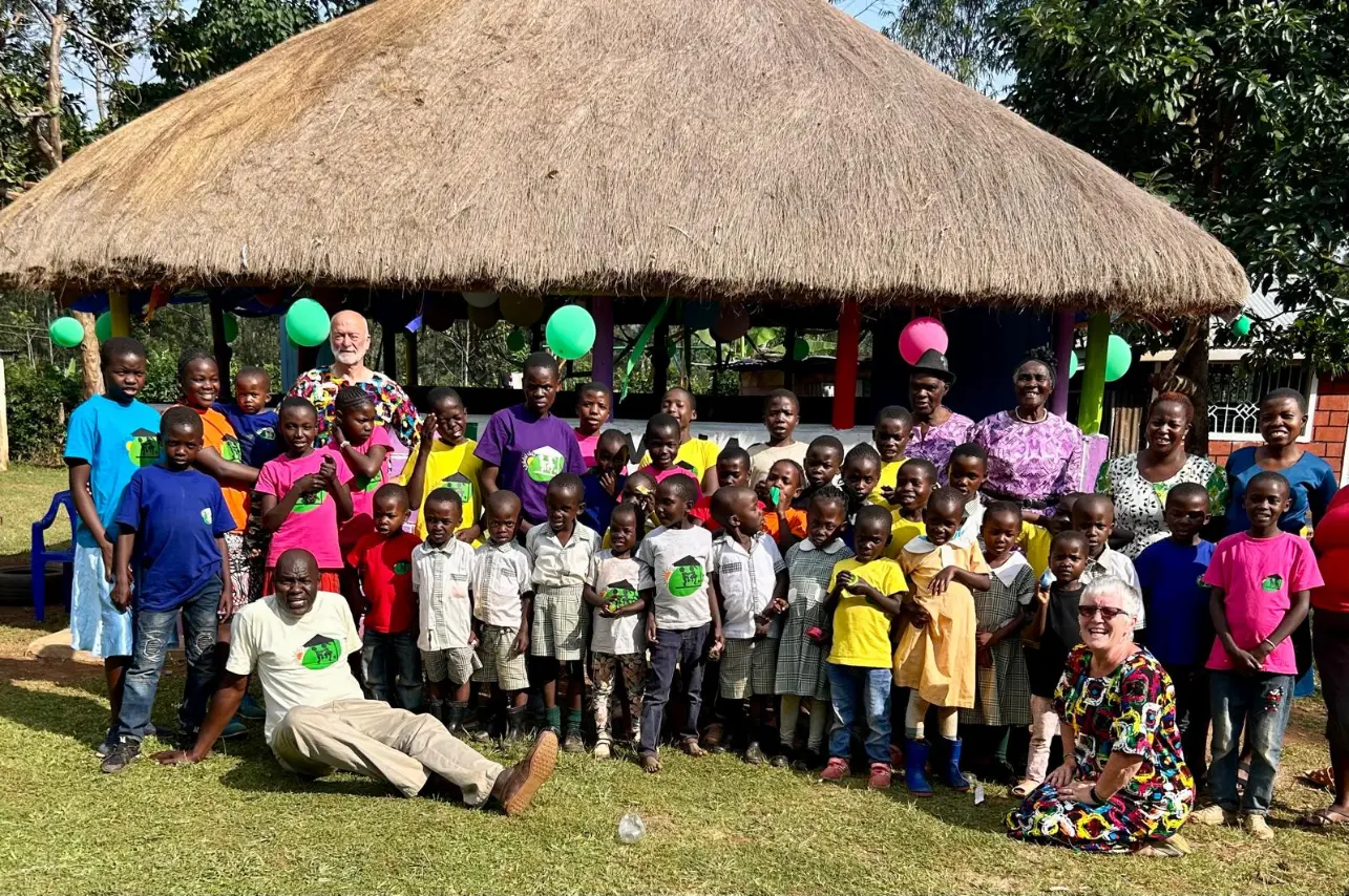 Volunteers and children at Green Village Hope Children Home in Vihiga, Kenya, group photo outside a thatched gazebo during a community day.